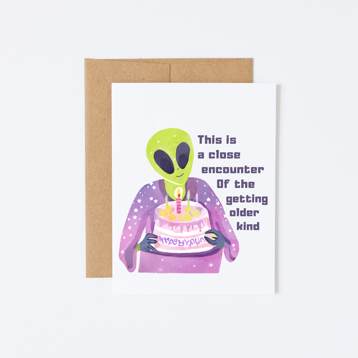 A white folding greeting card with an illustration of an alien holding a birthday cake